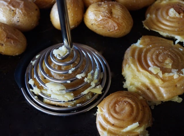 Yukon gold roasted potatoes with a potato smasher in black pan