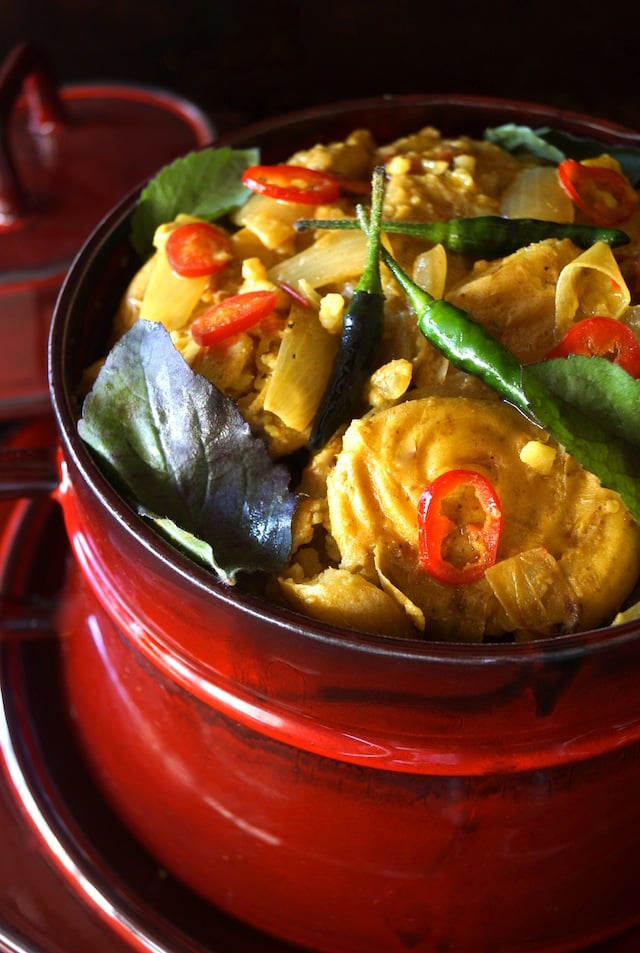 Curry Smashed Potato Stew Recipe in a bright red serving pot with lid in background and fresh green and red chiles on top.