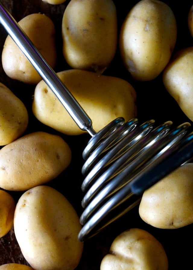 Raw Dutch Yellow Potatoes and a Smood potato smasher on a baking sheet.