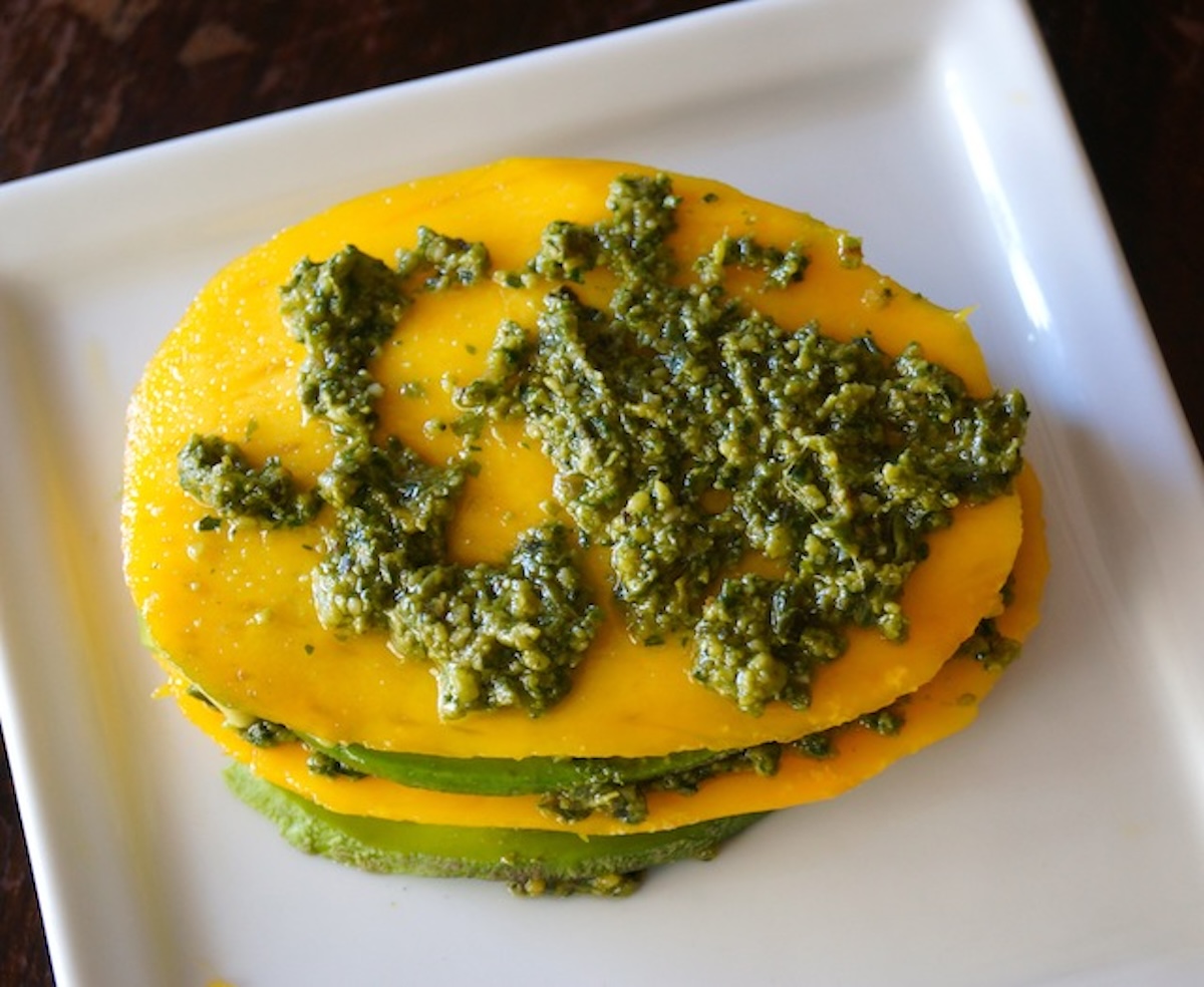 Stack of mango and avocado slices with pesto on top.