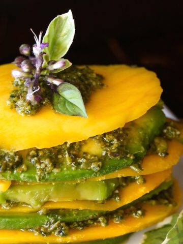 Mango Avocado Pesto Stack Recipe on a white plate with a purple basil flower on top.
