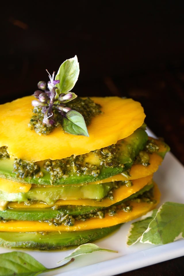 Mango Avocado Pesto Stack Recipe on a white plate with a purple basil flower on top.