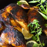 super browned chicken under a brick with fresh herbs in black pan
