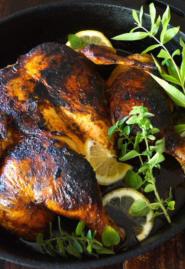 Lemon Herb Chicken Under a Brick Recipe in a cast iron skillet with fresh herbs.