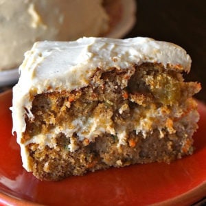 Big slice of gluten-free carrot cake with cardamom cream cheese frosting on a red plate.