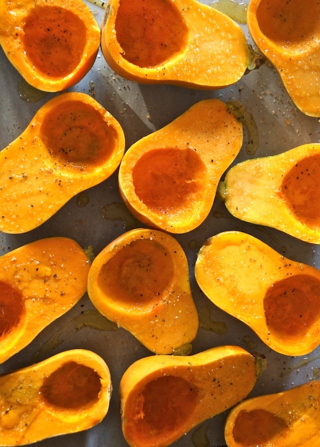 several honeynut squash, sliced in half on parchemnt, skin side down