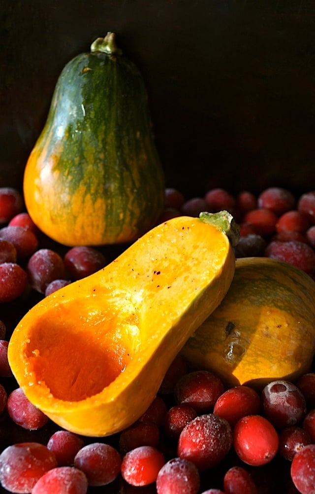  Caramelized Onion-Bacon and Cranberry Honeynut Squash - one green honeynut squash in background of an orange one sliced in half on cranberries.