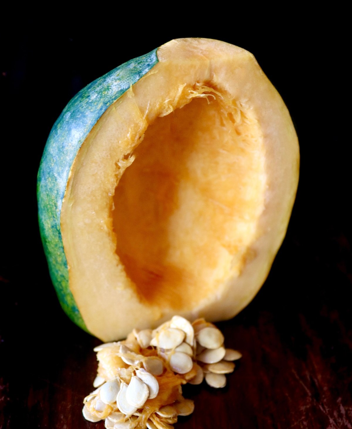 Half an acorn squash with seeds removed on black background.