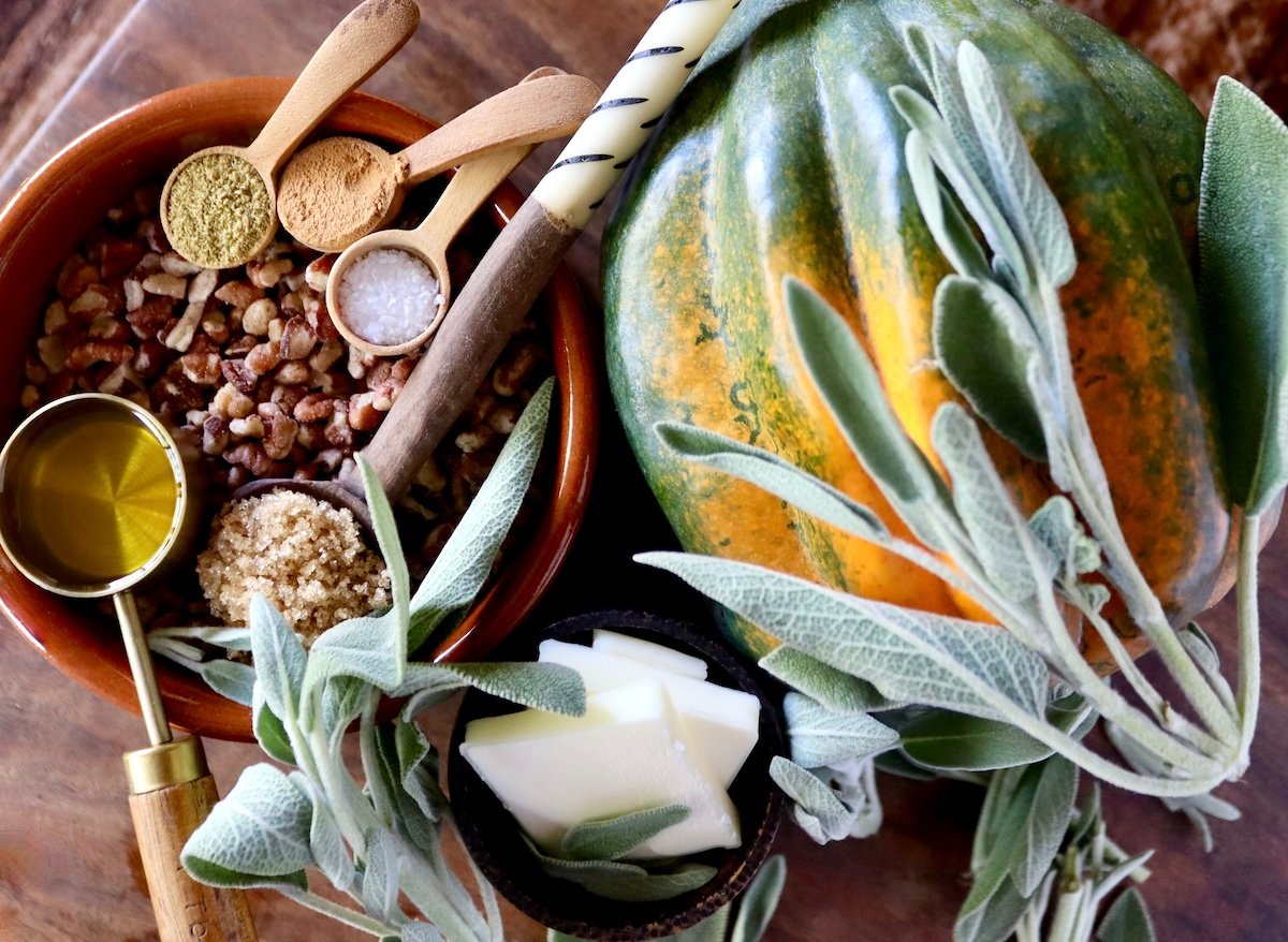 1 acorn whole raw squash with fresh sage and a terra cotta dish with pecan pieces and spices.