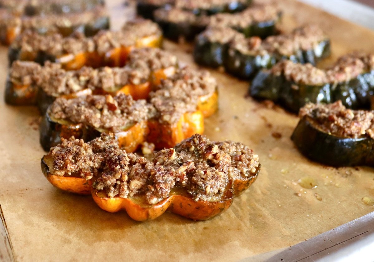 Several slices of pecan-crusted acorn squash on a parchment lined baking sheet.