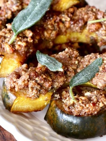 White plate with several slices of baked acorn squash topped with a pecan crust.