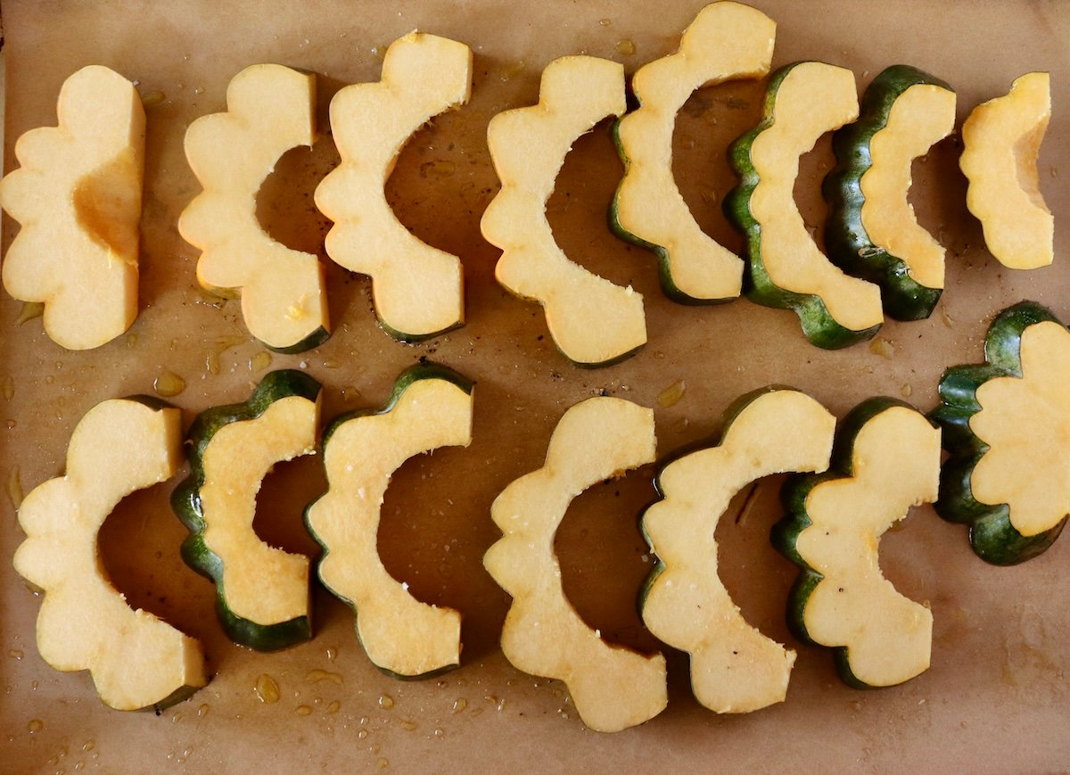 Several slices of acorn squash on a parchment-lined baking sheet.