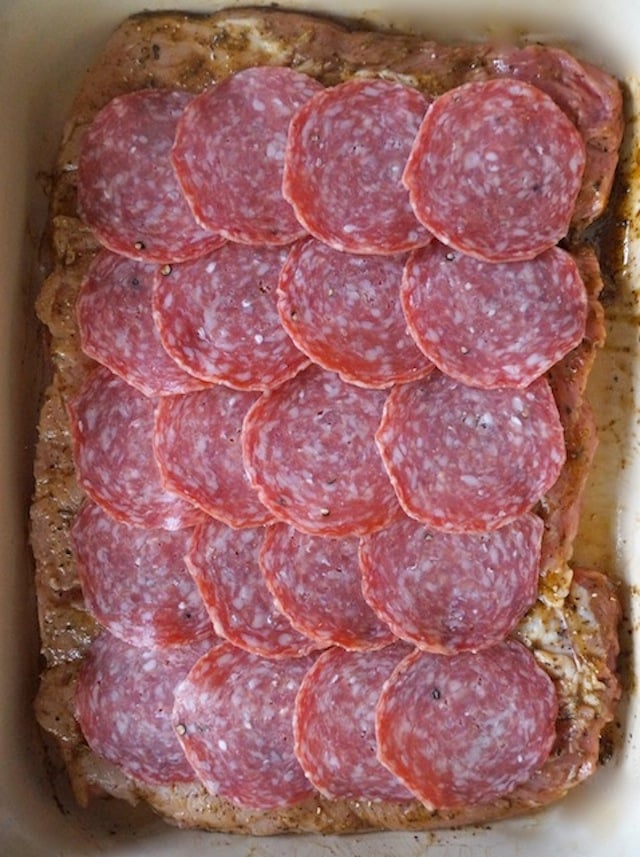 sliced salami in layers on top of butterflied pork loin