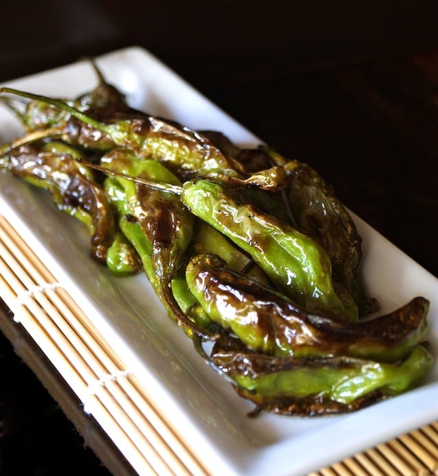 blistered shishito peppers on a narrow white plate