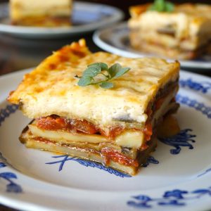 Square piece of potato moussaka on a whte plate with blue flowers