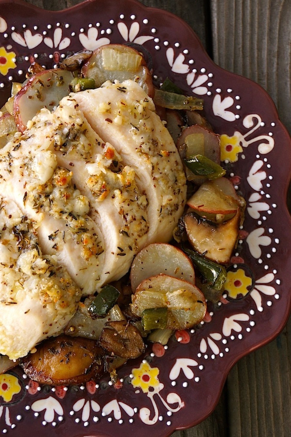 Deep purple plate with painted edges with sliced Parmesan-Crusted chicken breast and roasted potatoes.