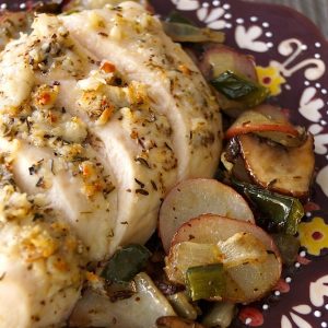 Deep purple plate with painted edges with sliced Parmesan-Crusted chicken breast and roasted potatoes.