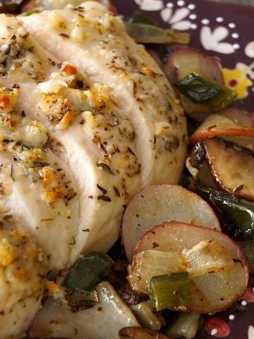 Deep purple plate with painted edges with sliced Parmesan-Crusted chicken breast and roasted potatoes.