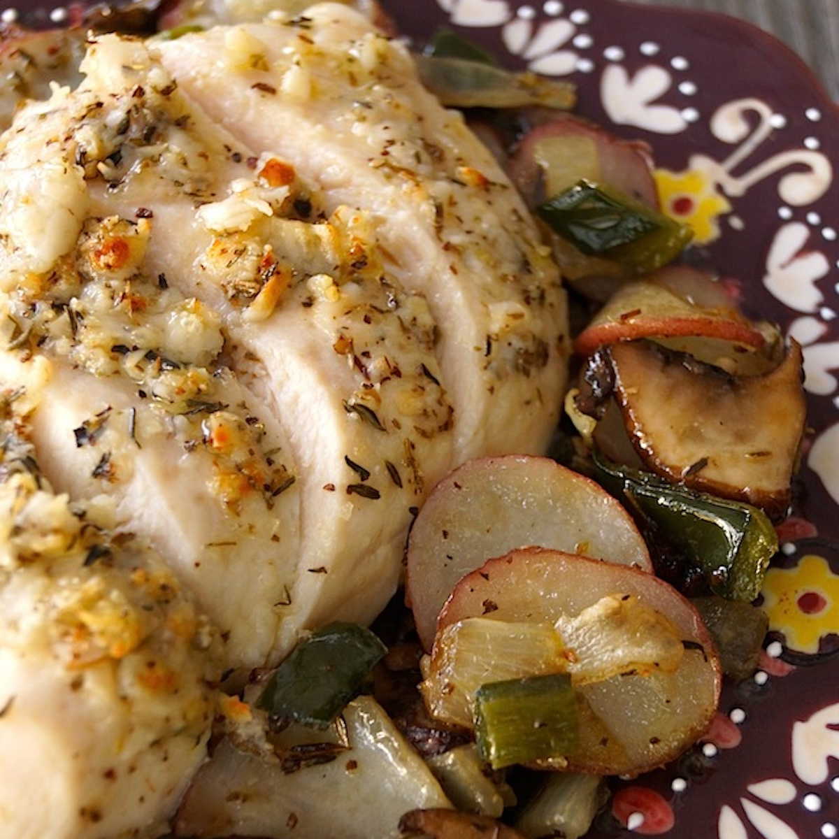 Deep purple plate with painted edges with sliced Parmesan-Crusted chicken breast and roasted potatoes.