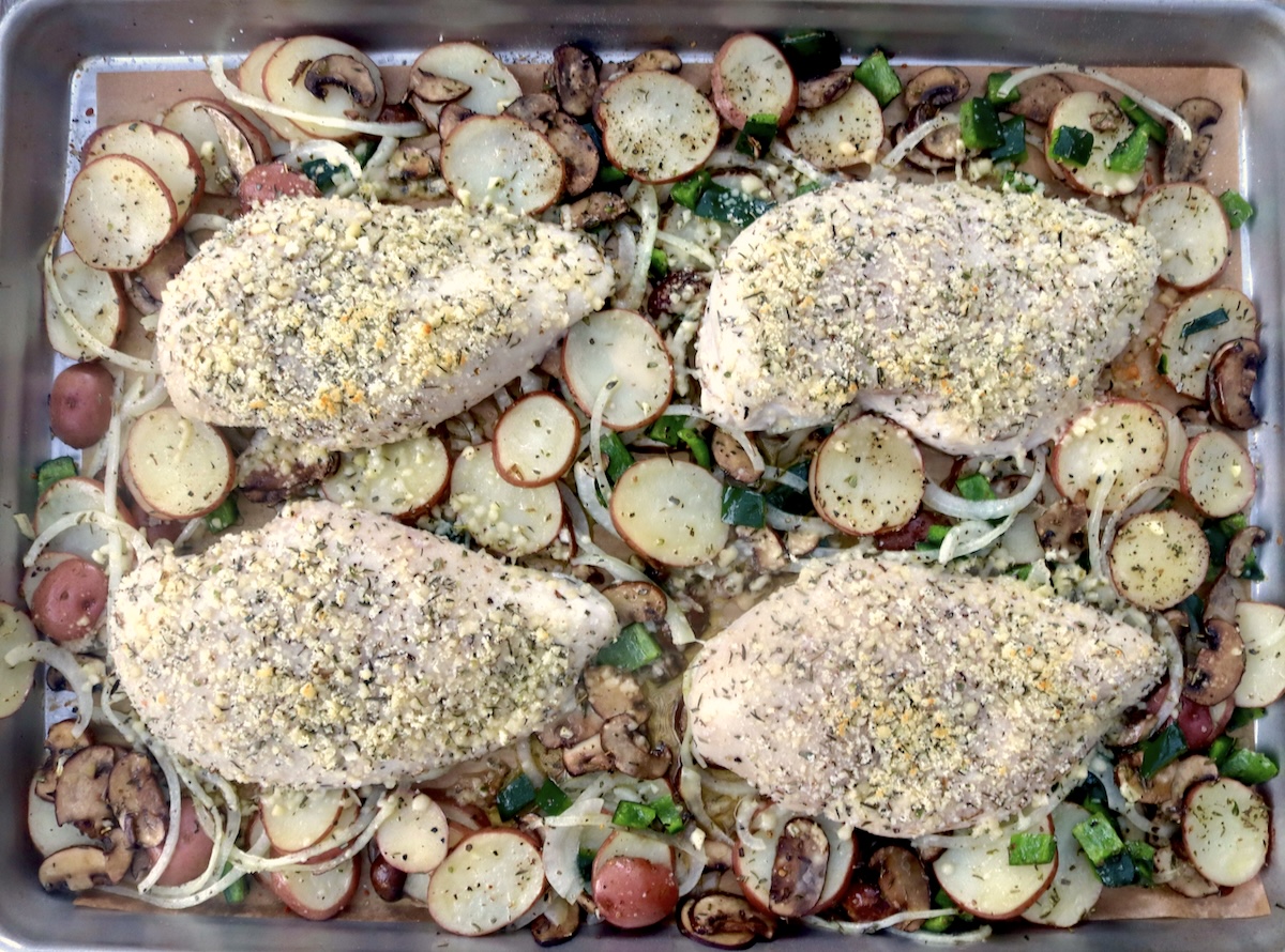 Sheet pan with 4 parmesan-coated chicken breasts and vegetables.