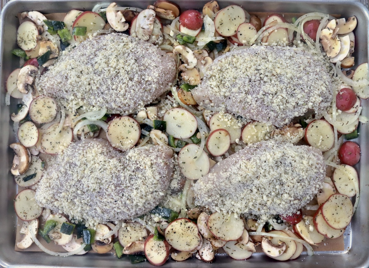 Sheet pan with 4 parmesan-coated, raw chicken breasts and vegetables.