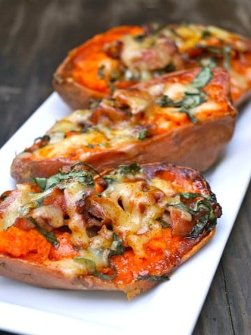 Bacon Basil Baked Sweet Potatoes with melted cheese on top on a white plate.