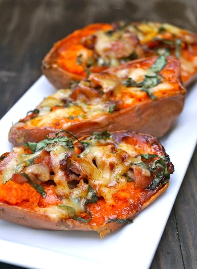 3 halves of Baked Basil Sweet Potatoes with bacon on a white narrow dish.