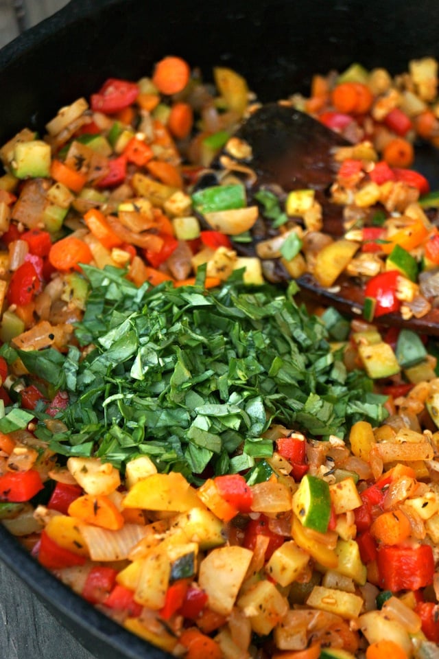Vegetables and fresh basil are brightly colored and mixed in a cast iron skillet