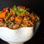 A cream colored bowl of Smoky Lemon Vegetable Quinoa with a black background.