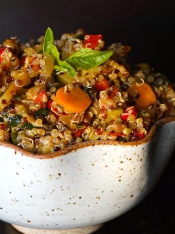 A cream colored bowl of Smoky Lemon Vegetable Quinoa with a black background.