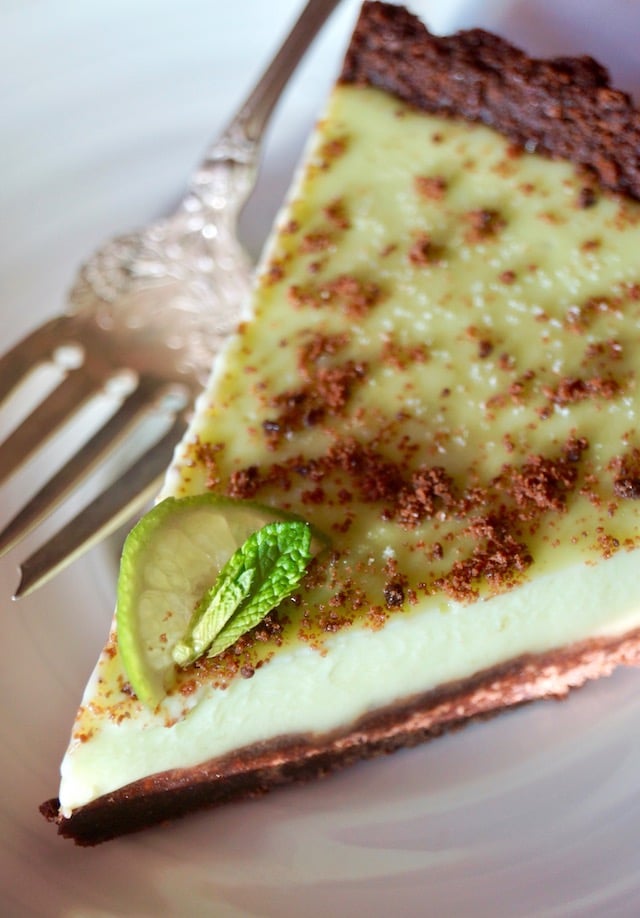 One slice of Thin Mint Key Lime Tart with a small lime slice and mint leaf, on white plate with silver fork.