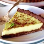 A perfect slice of Key Lime Pie with a chocolate mint cookie crust, with a silver fork on a white plate.