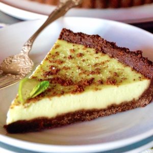 A perfect slice of Key Lime Pie with a chocolate mint cookie crust, with a silver fork on a white plate.