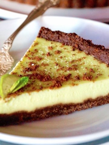 A perfect slice of Key Lime Pie with a chocolate mint cookie crust, with a silver fork on a white plate.