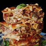 Three stacked square slices of lamb lasagna on a white and blue pretty china small plate.