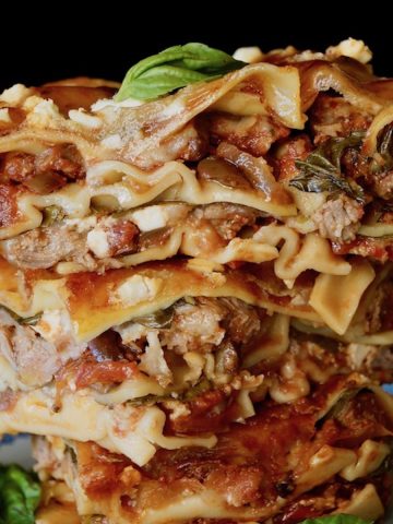 Three stacked square slices of lam lasagna on a white and blue pretty china small plate.