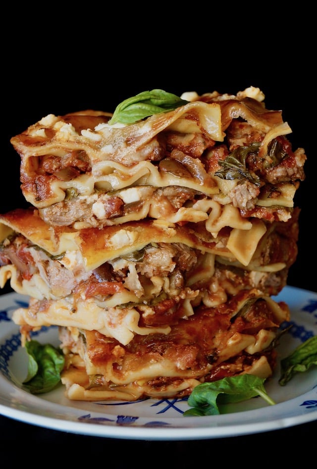 three big pieces of lamb Lasagna stacked on top one another with fresh basil leaves