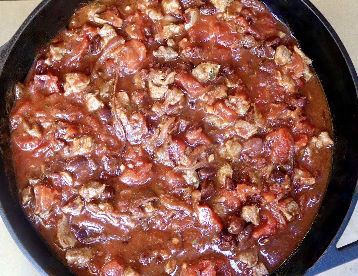 Lamb-Lasagna-Recipe Cast iron skillet with sliced, cooked red onions, lamb and tomato sauce.