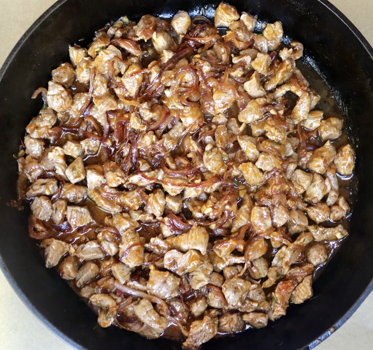 Lamb-Lasagna-Recipe Cast iron skillet with sliced, cooked red onions, and slightly cooked marinated chunks of lamb.