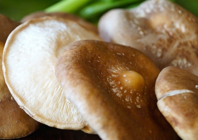 A few whole shiitake mushrooms with green behind them.