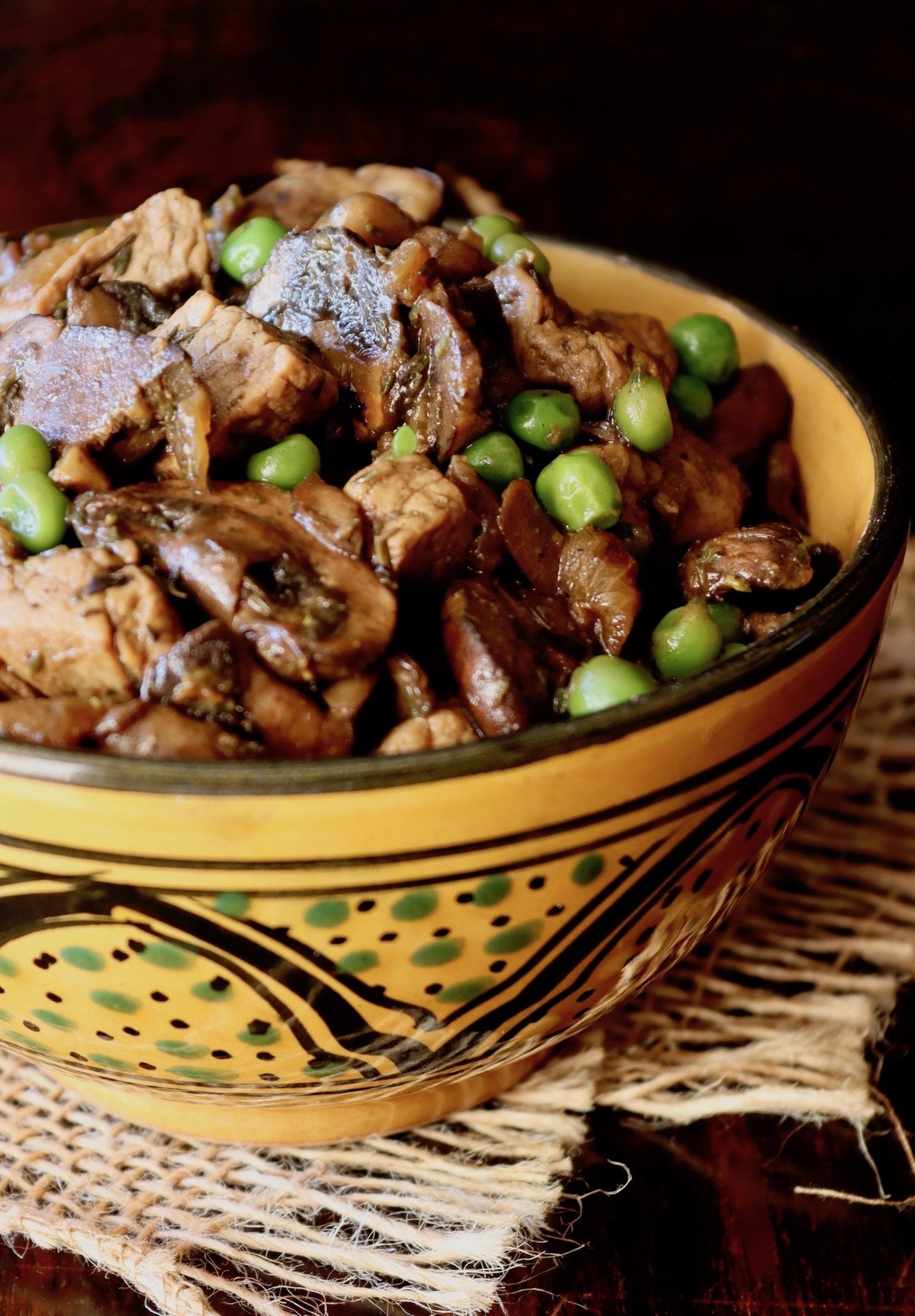 Mushroom and Pork Stew in a gold bowl with black rim, on dark wood surface.