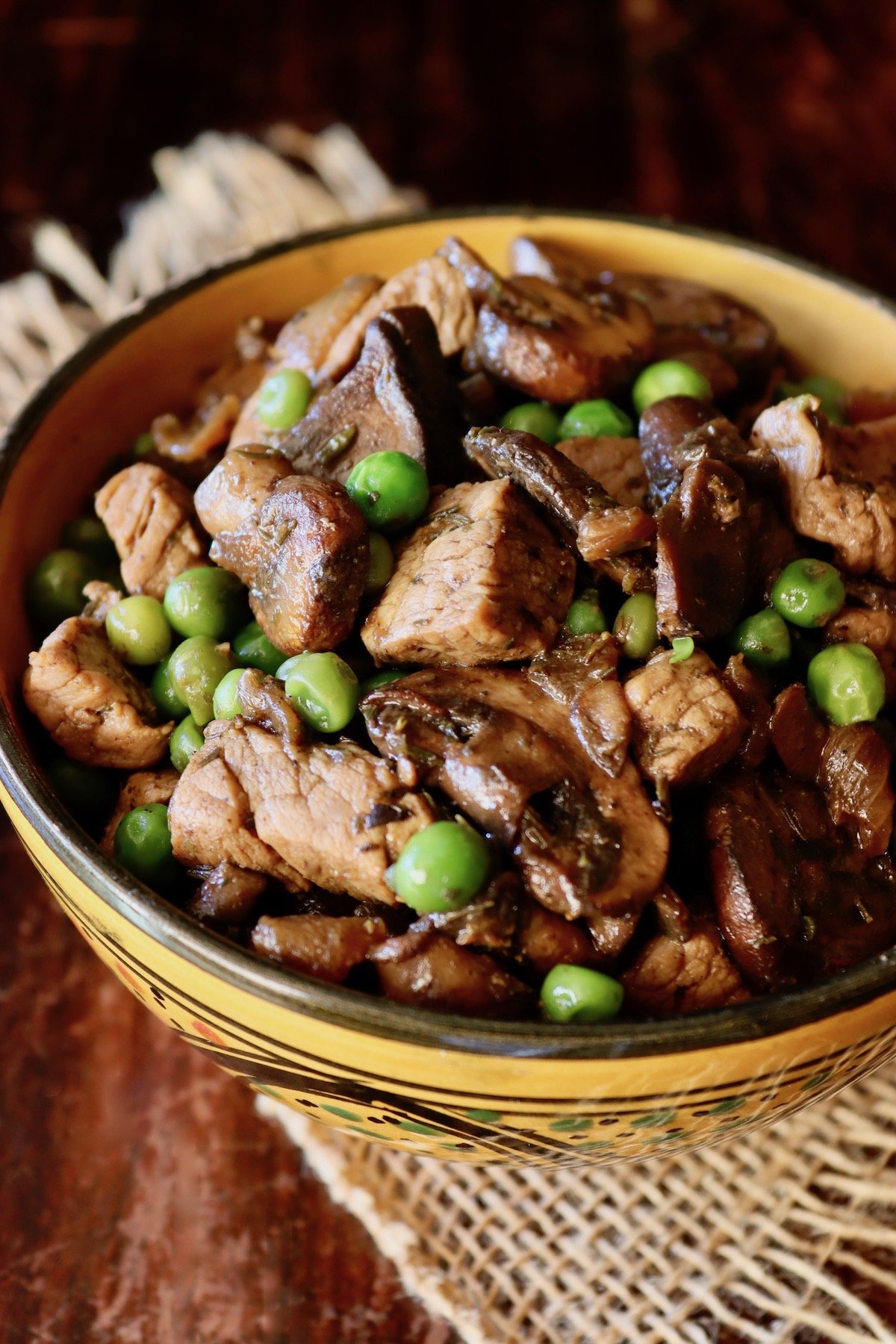 Top view of Mushroom Pork Stew in a gold bowl with black top rim, on dark wood surface.