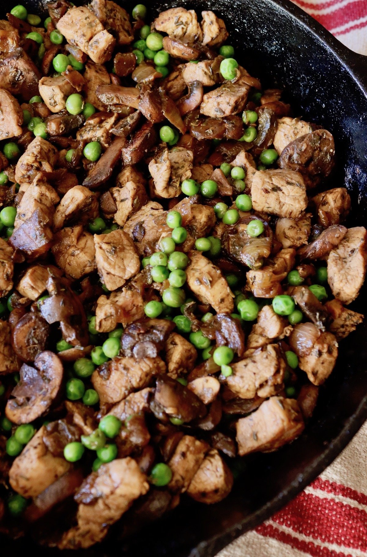 Large cast iron skillet with pork, mushrooms and peas.