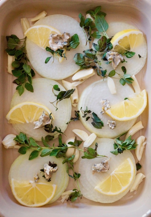 onion and lemon slices, garlic and oregano sprigs in a baking dish