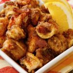 White square bowl full of fried calamari with bits of bacon.