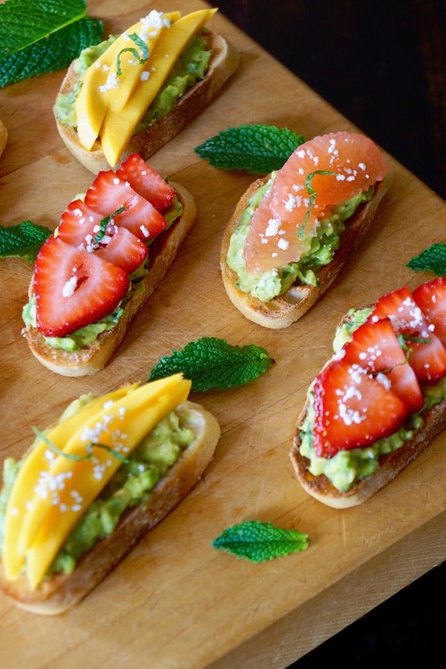 Avocado Toast with Mint and Fruit on cutting board with strawberry, mango and grapefruit