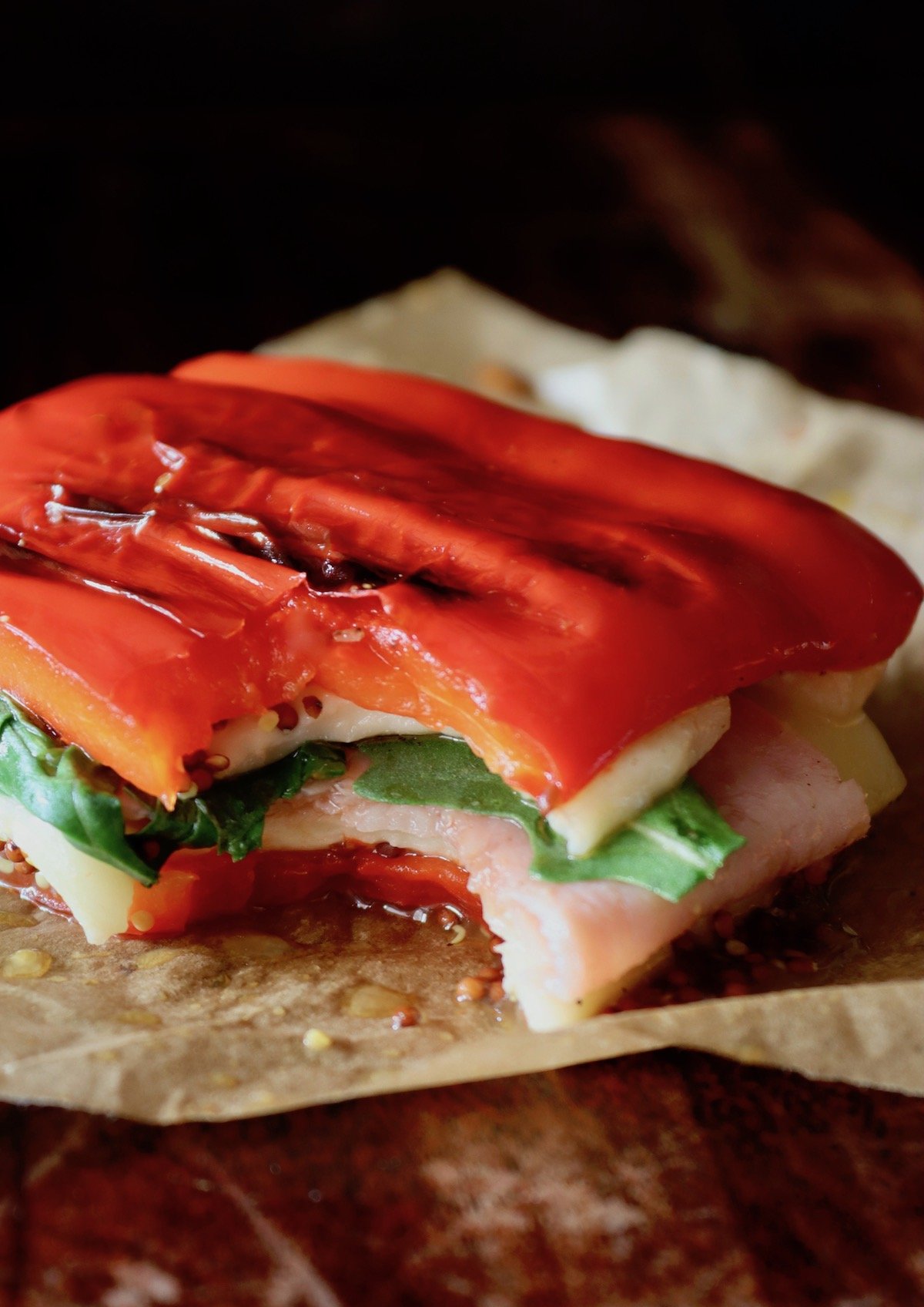 grilled red bell pepper sandwich on parchment with one bite missing