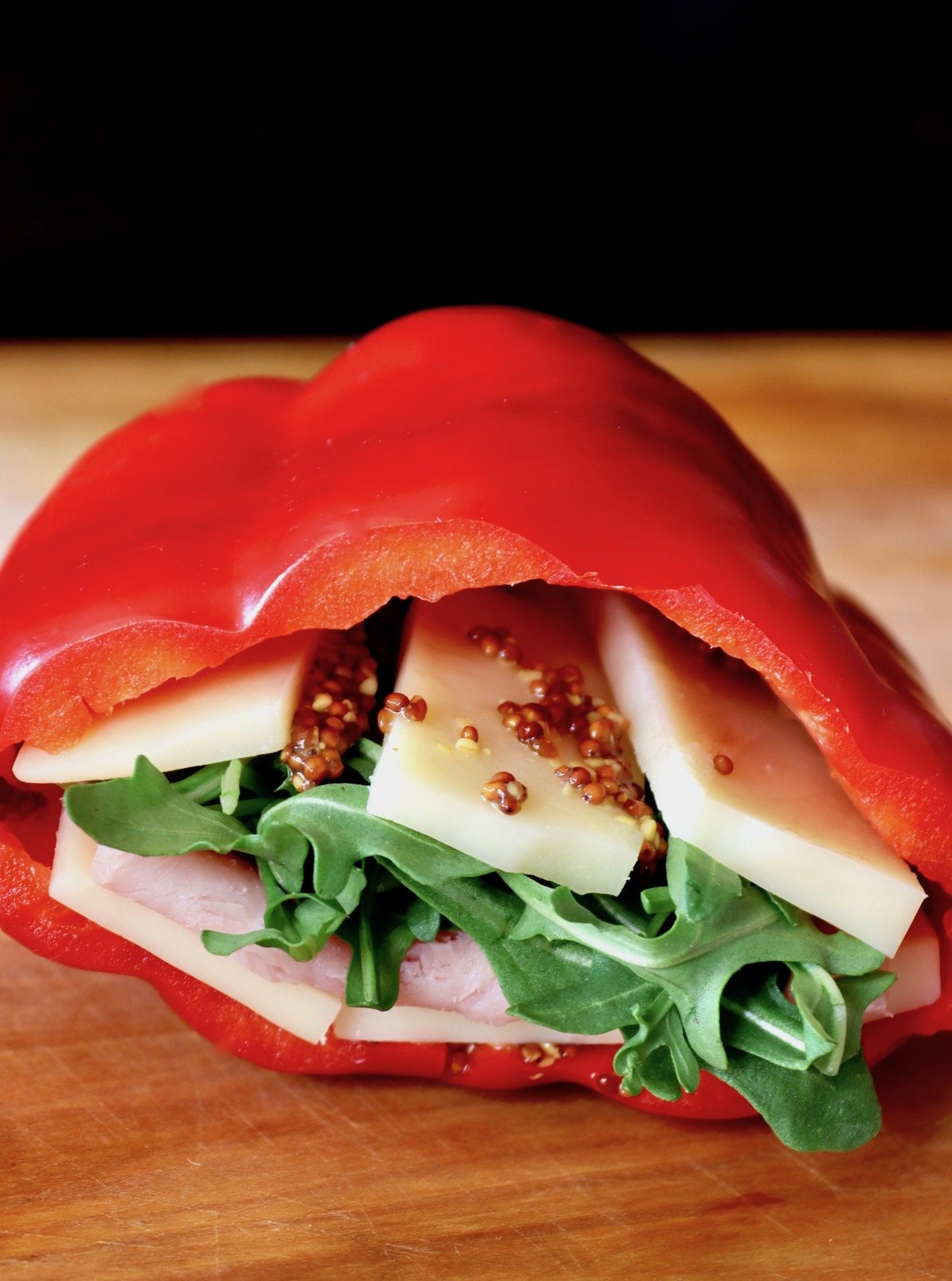 Red bell pepper filled with cheese lettuce and ham on cutting board