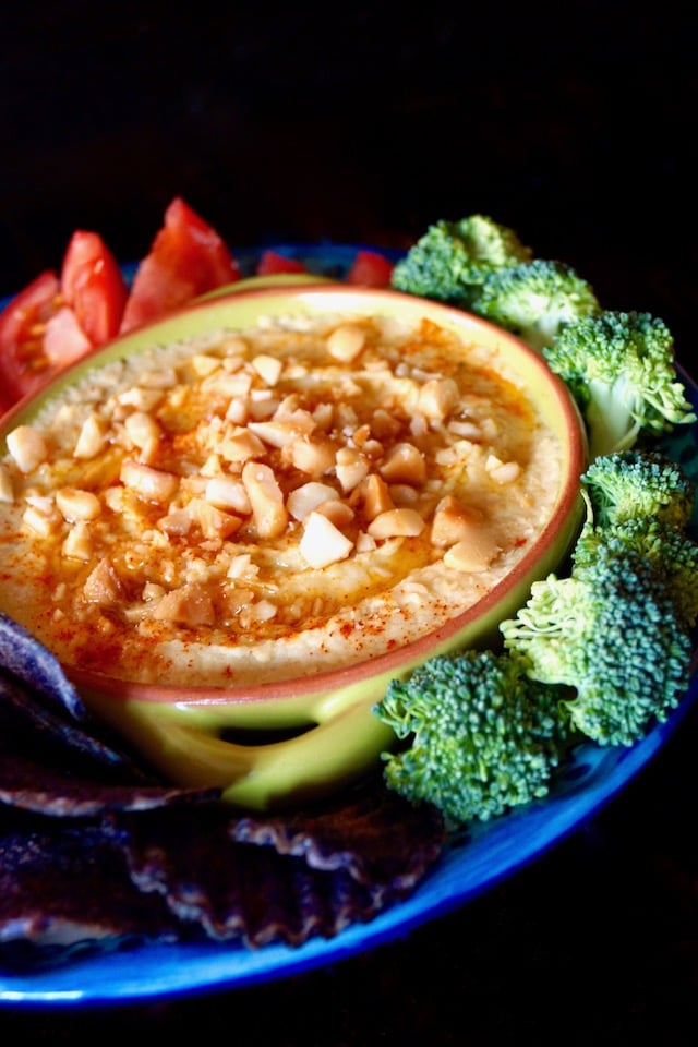 Roasted Macadamia Nut Hummus in green bowl surround by broccoli and tomatoes