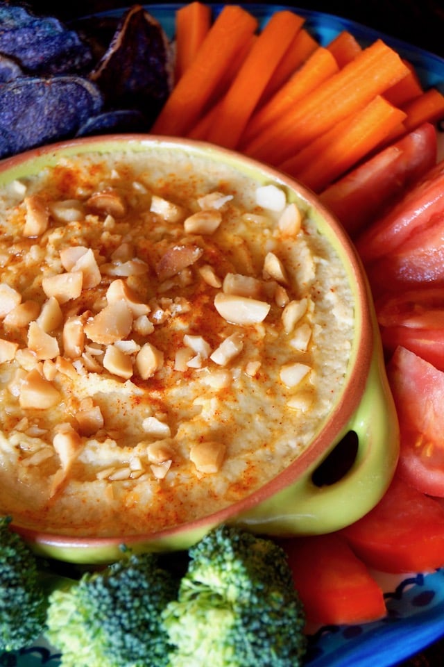 Roasted Macadamia Nut Hummus in a green bowl, surrounded by raw vegetables